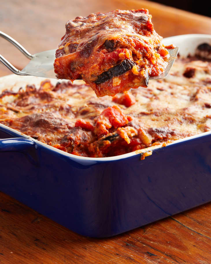 Eggplant parmesan in blue baking dish with piece sliced out on a serving spatula.