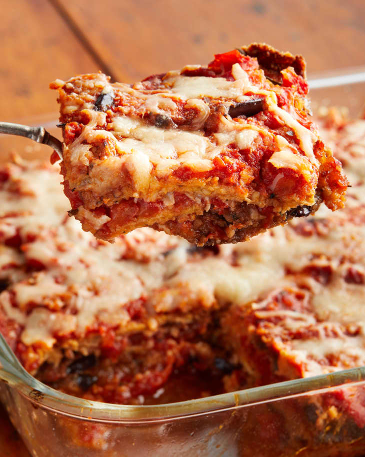 Baked eggplant parmesan in glass baking dish with piece scooped out on serving utensil.