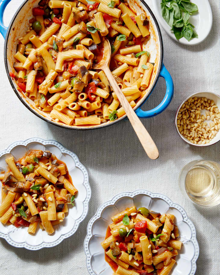 The eggplant caponata pasta is served on to scalloped plates from a large dutch oven.