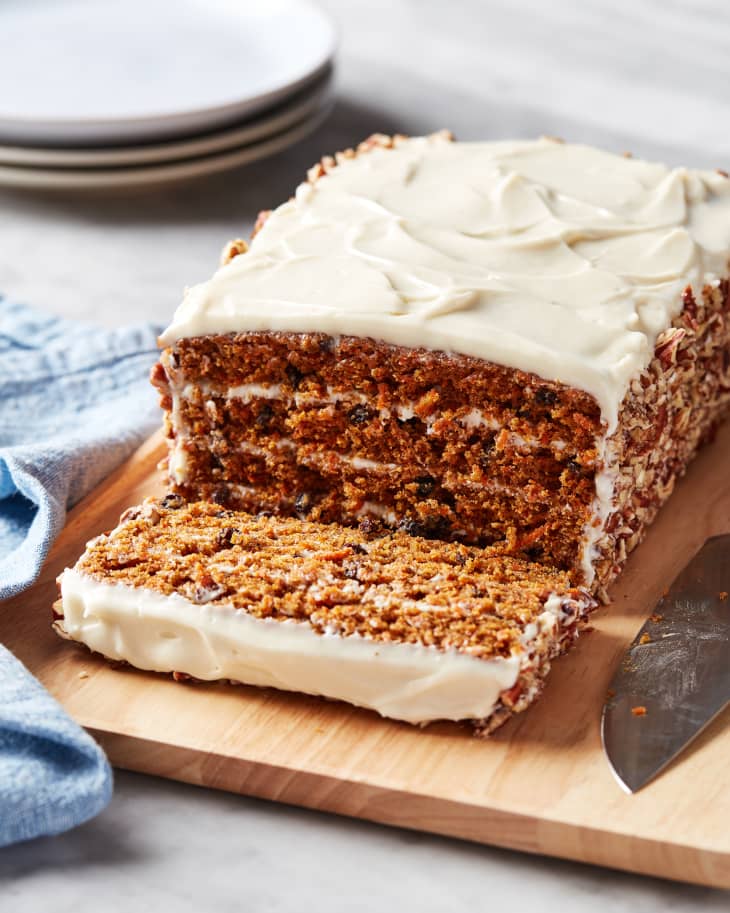 Cook's Illustrated carrot cake on wooden cutting board with one piece sliced.