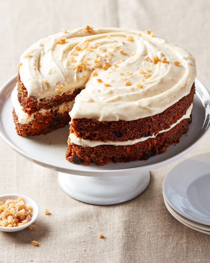 Ina Garten's carrot cake on cake stand with piece sliced out.