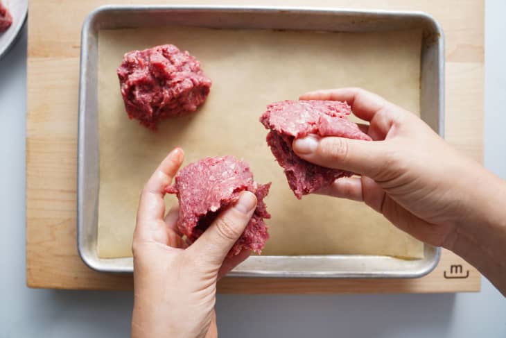 Ground beef hunks are smashed with a spatula during cooking to make smash burgers.