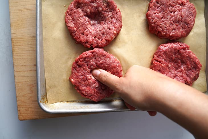 Burger patty is shaped and a thumb is pressed into the center to make a small indentation.