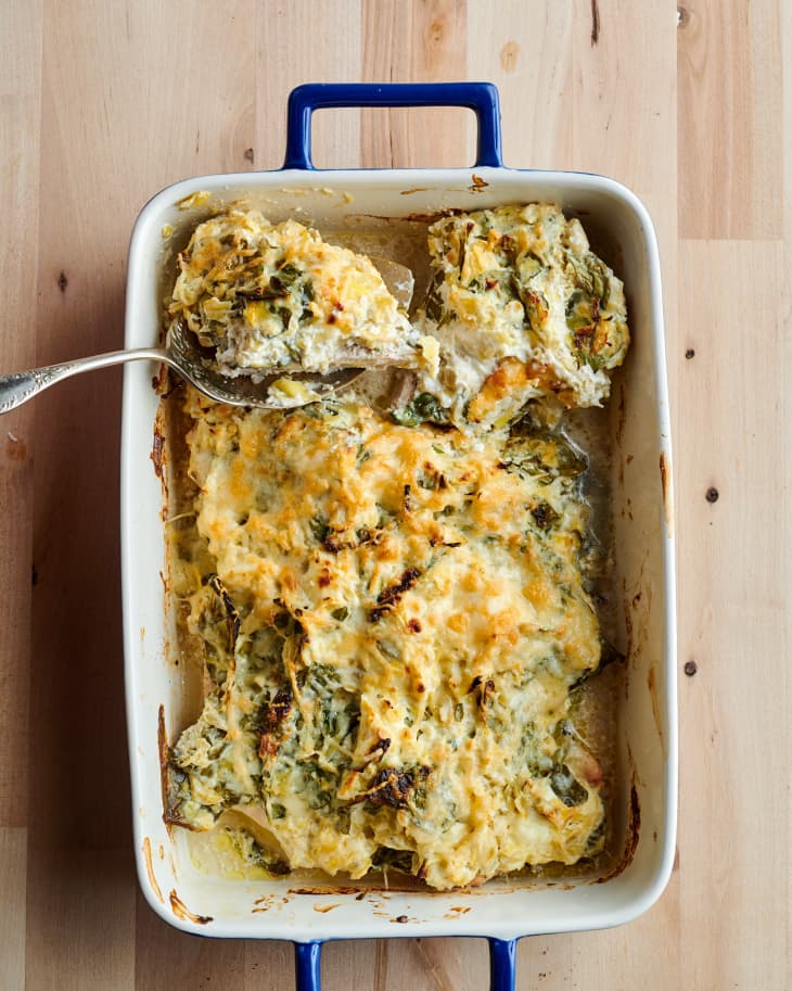 Spinach artichoke baked chicken lifted from baking dish with serving spoon.