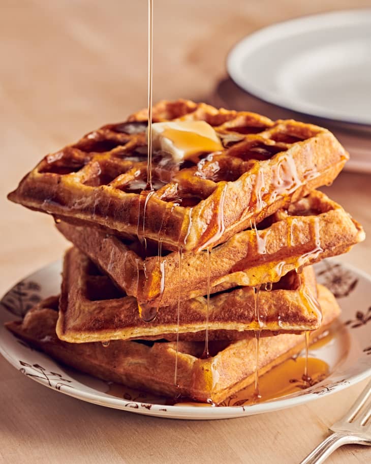 Syrup is poured over a stack of four waffles.