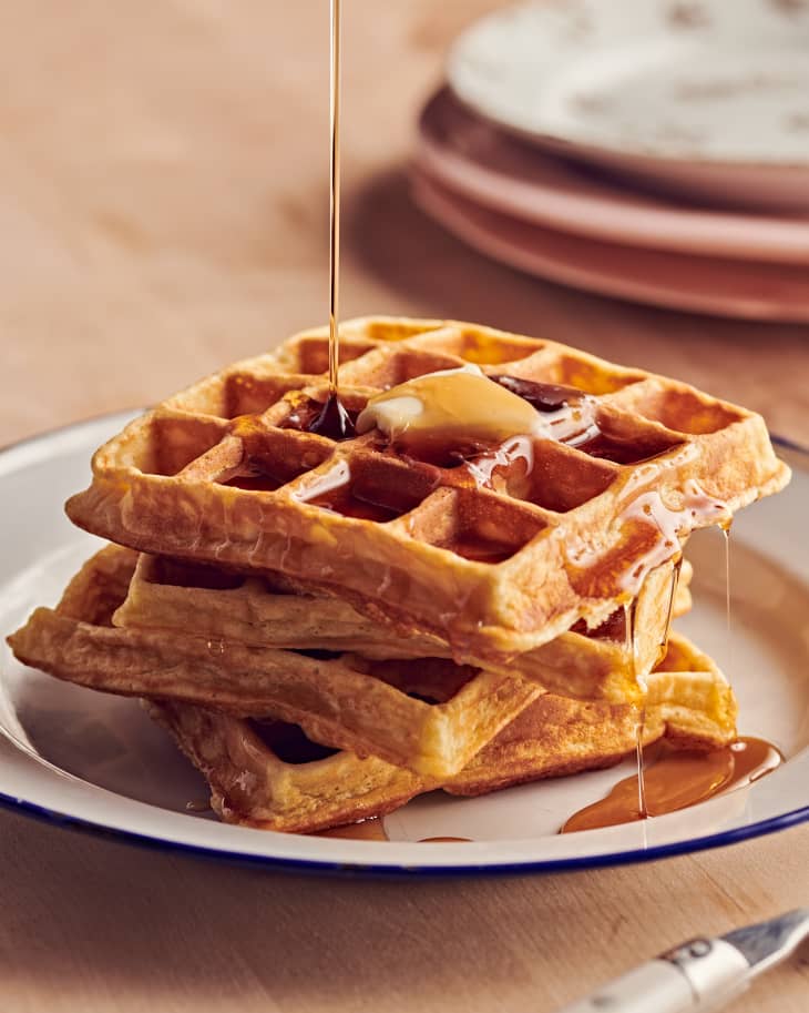Three waffles stacked on a plate with syrup poured on them