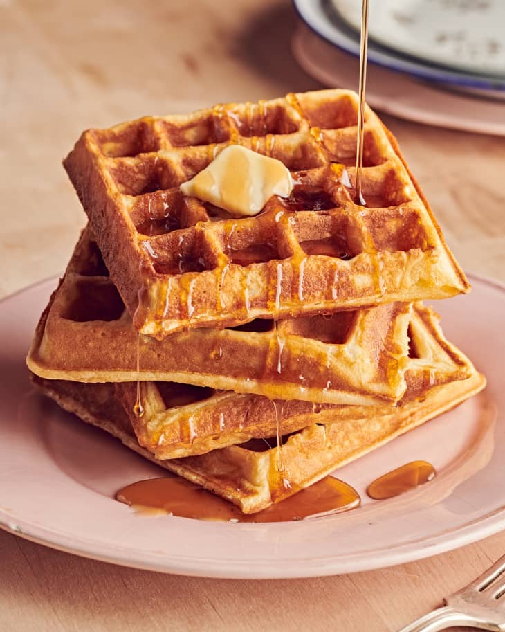 four waffles stacked with syrup being drizzled over them