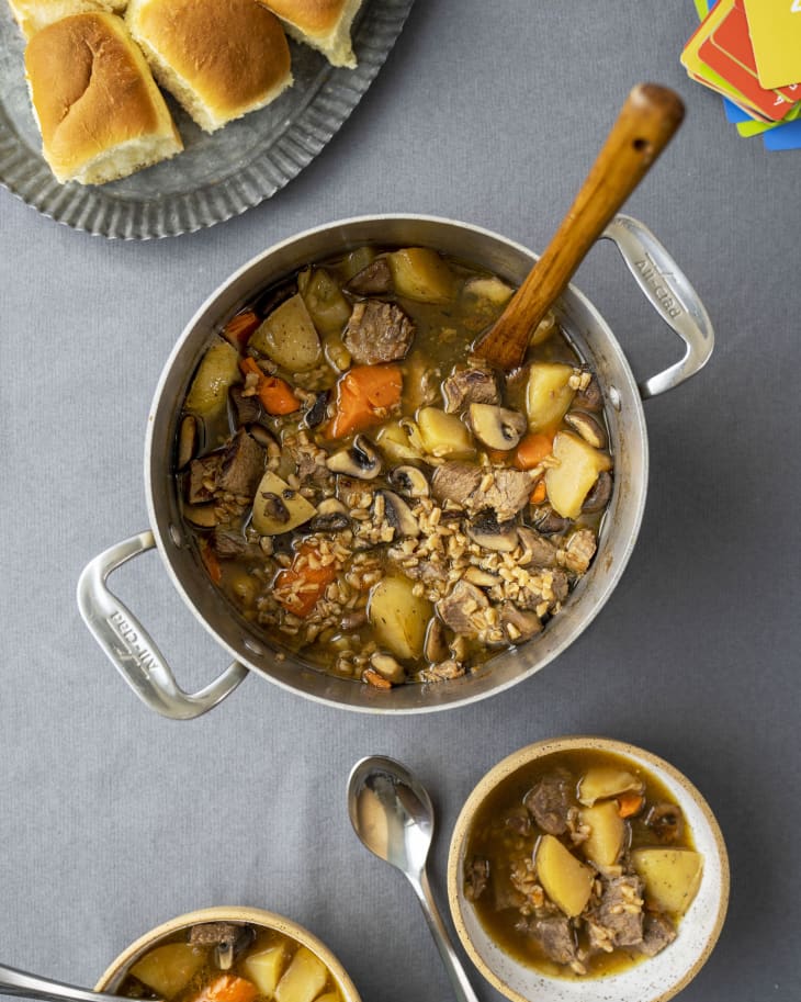 Large pot with beef and barley soup in it with small bowls and rolls near