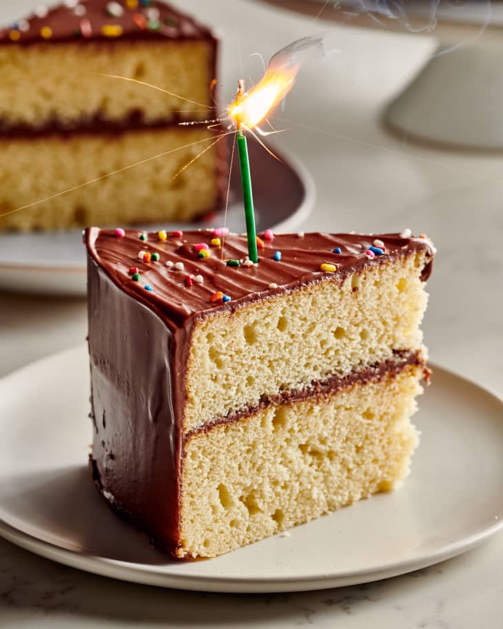 slice of birthday cake sits with lit candle on top