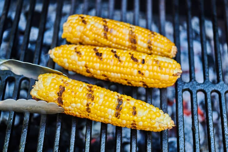 Three ears of corn, without husks, are being grilled on an outdoor grill.