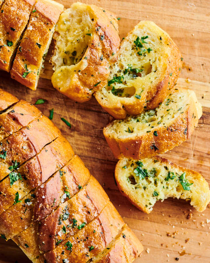 slices of the garlic bread sit next to a garnished, scored loaf
