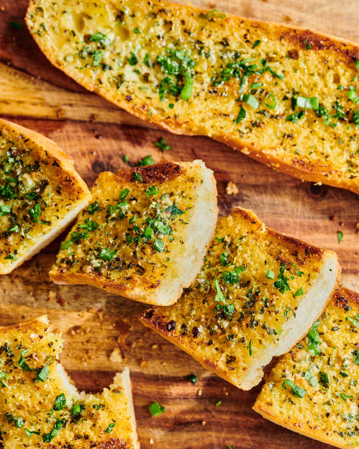 slices of garlic bread sit next to a whole loaf on wood