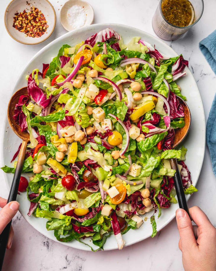 someone is ready to eat, with knife and fork in hands, the italian chopped salad