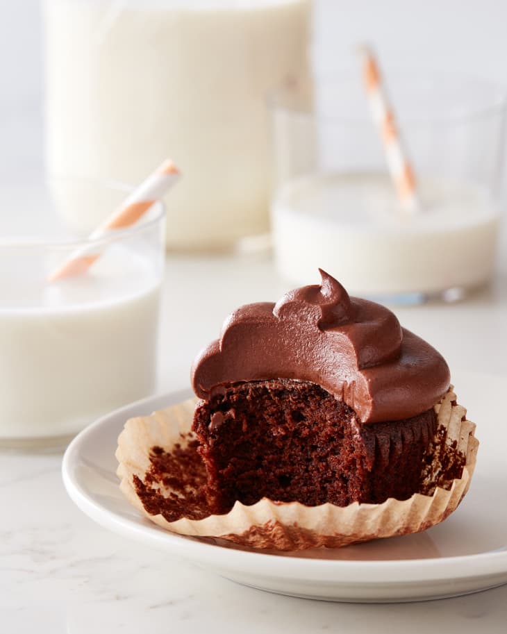 chocolate cupcake with a bite taken out of it sits on a plate with glasses of milk in the background