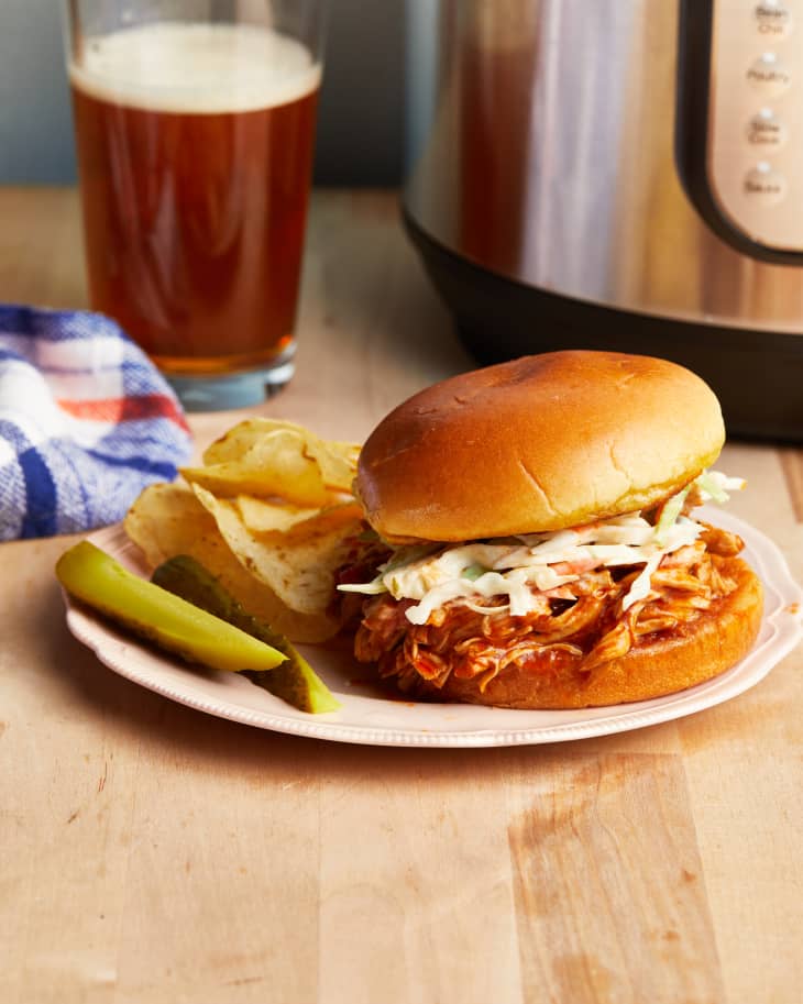 bbq chicken sandwich sits on a plate with pickle spear and chips