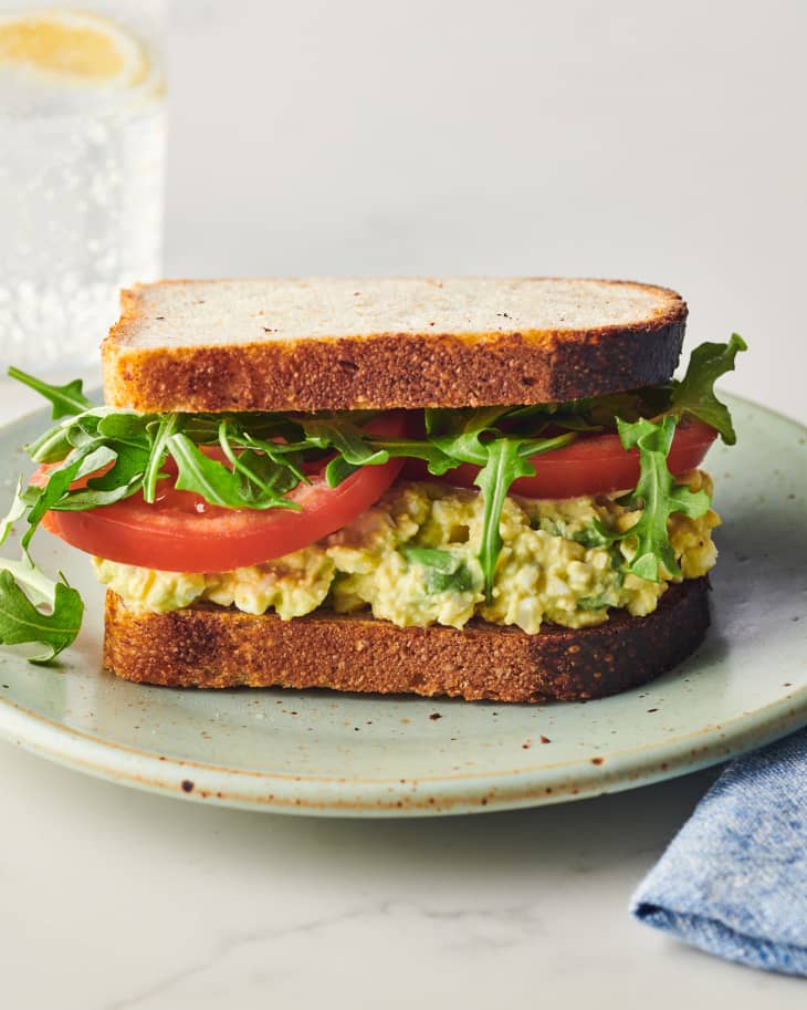egg salad on a sandwich with tomato and greens