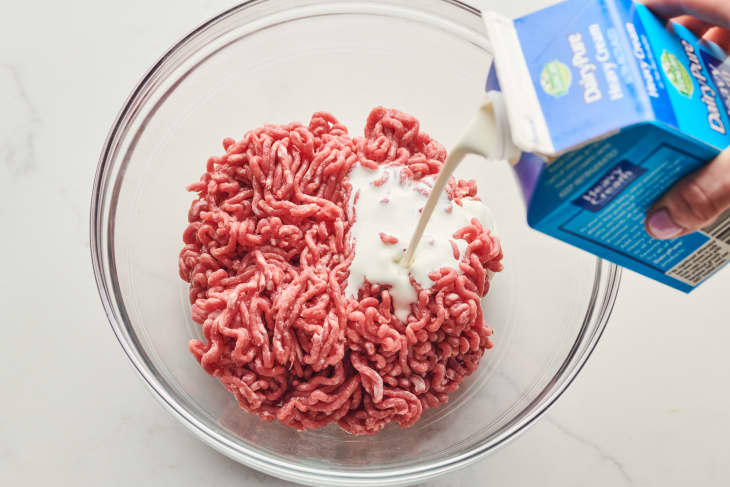 someone is adding cream to a bowl of raw ground beef