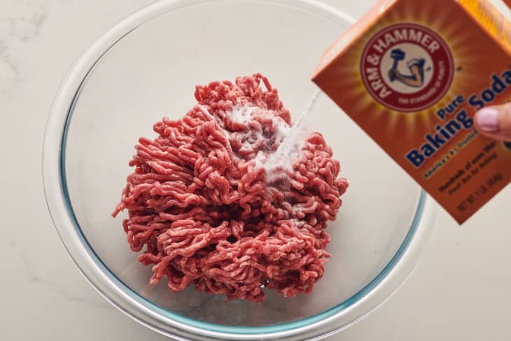 someone is adding baking soda to a bowl of raw ground beef