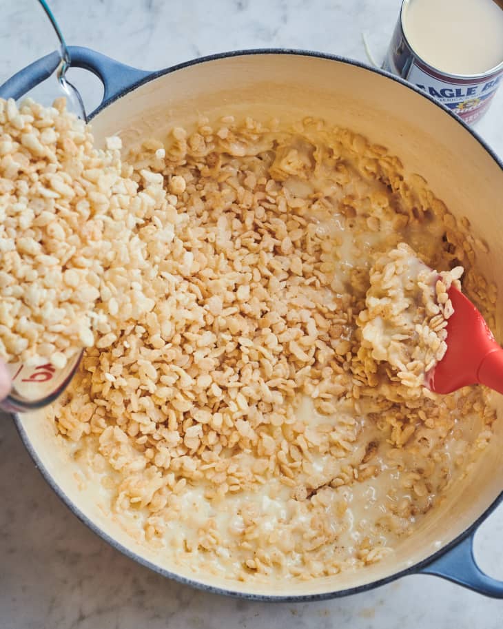 someone is pouring rice krispies into pot with marshmallow and other rice krispies