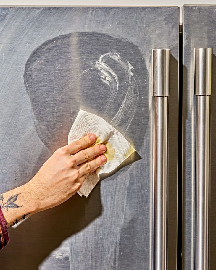 a hand wiping down a stainless steel refrigerator