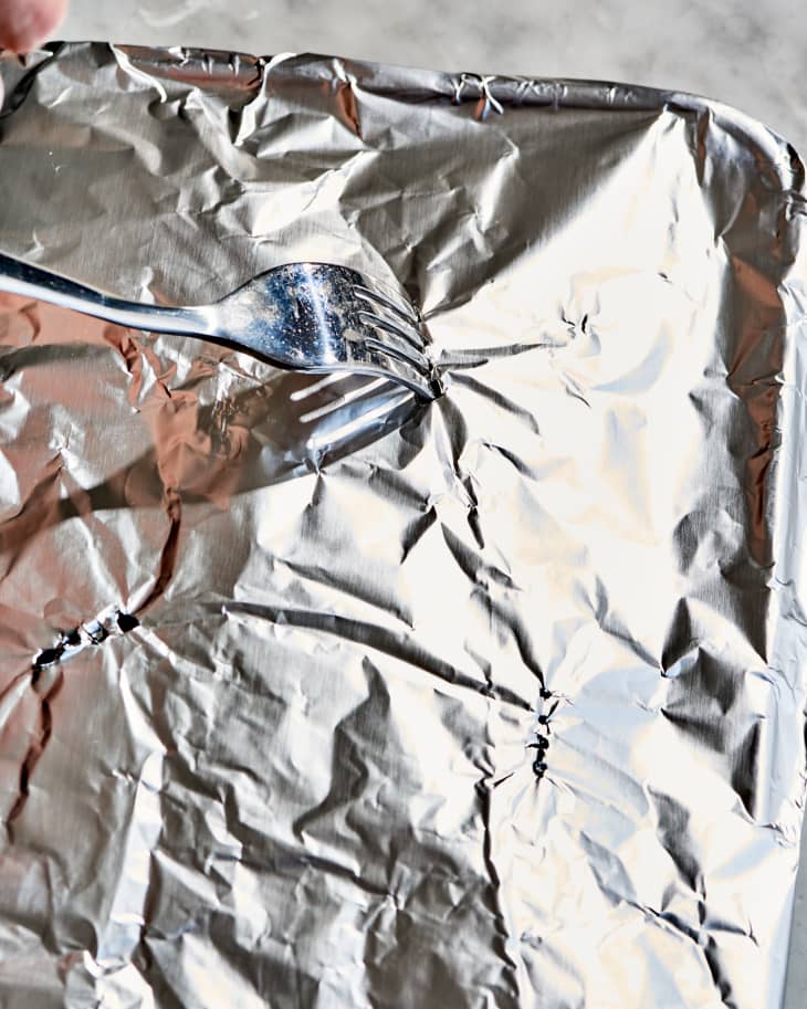 a fork poking holes in an aluminum foil covered sheet pan