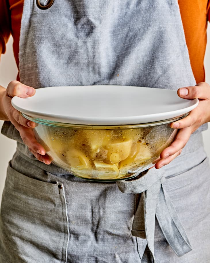 a person holding a glass bowl of parboiled potatoes
