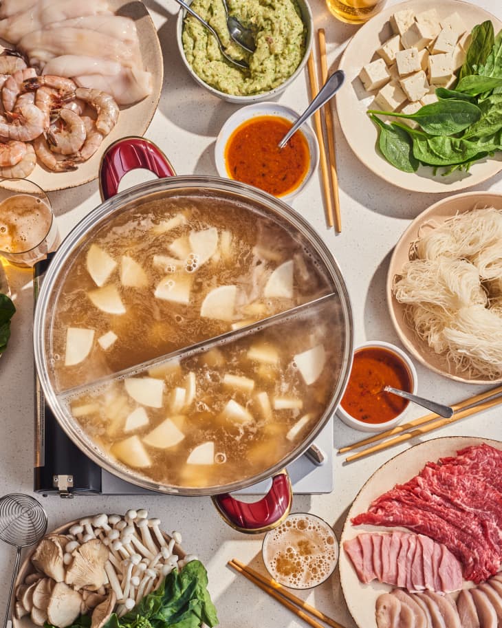 hot pot on table with things to cook in it nearby on plates