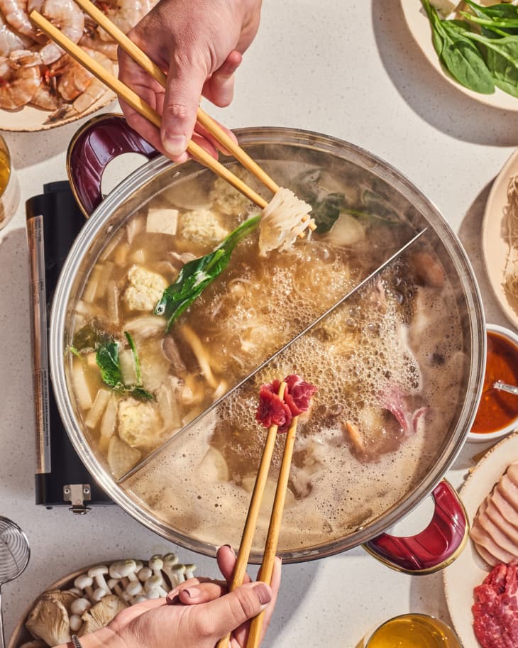 hot pot on table with things to cook in it nearby on plates