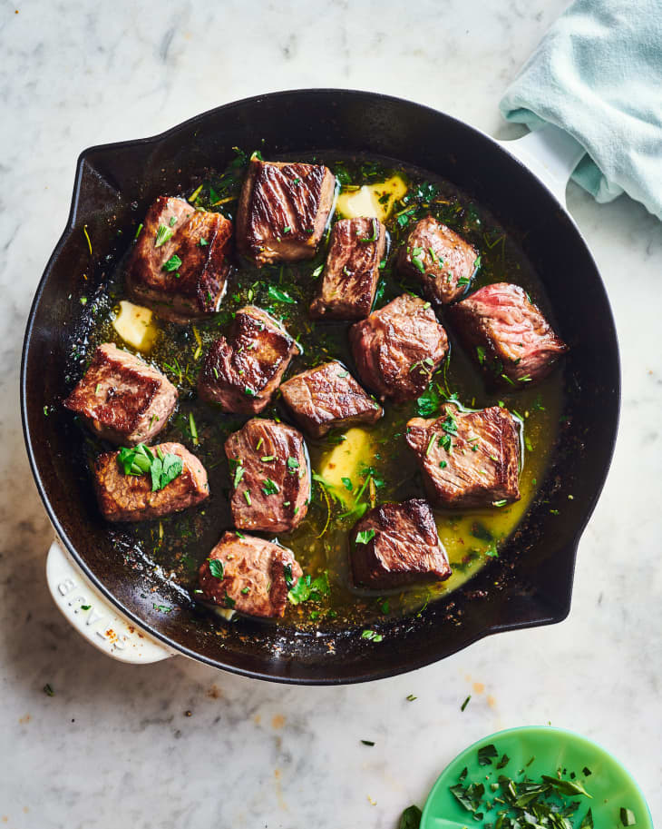 herb butter steak bites cooking in a cast iron skillet