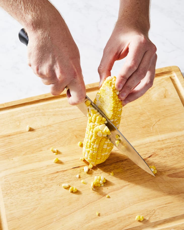 cutting corn with knife on cutting board