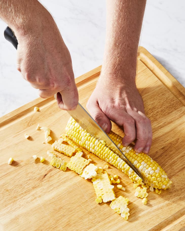 cutting corn with knife on cutting board