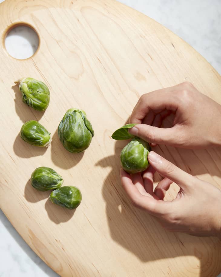 someone peeling sprouts on uctting board