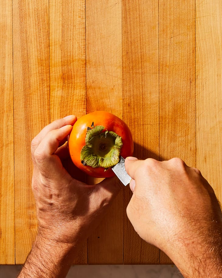 someone cutting the top of the persimmon off