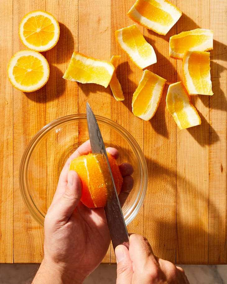 someone cutting an orange with a knife over a bowl