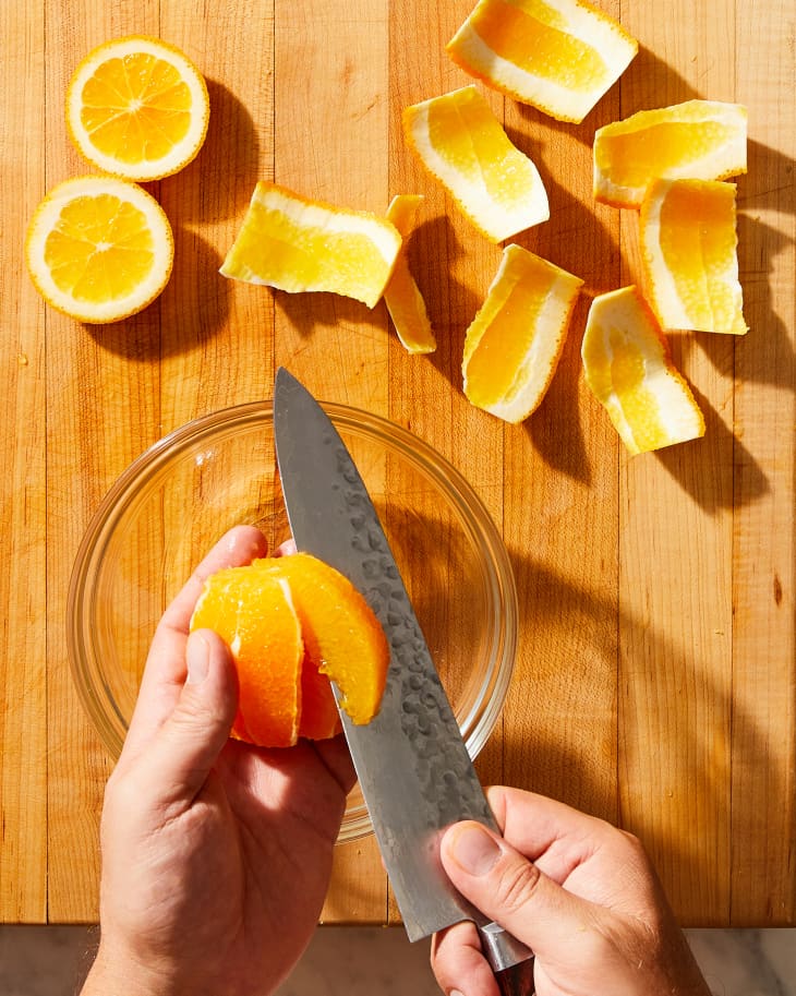 someone cutting an orange with a knife over a bowl