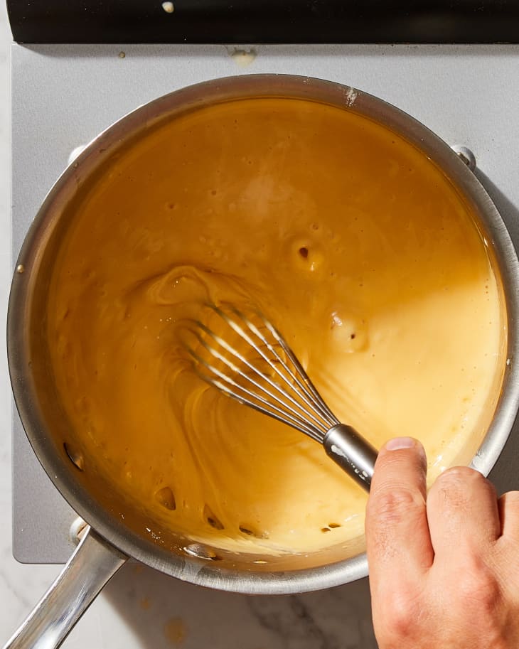 someone mixing cheese with a whist in a stainless steel pot