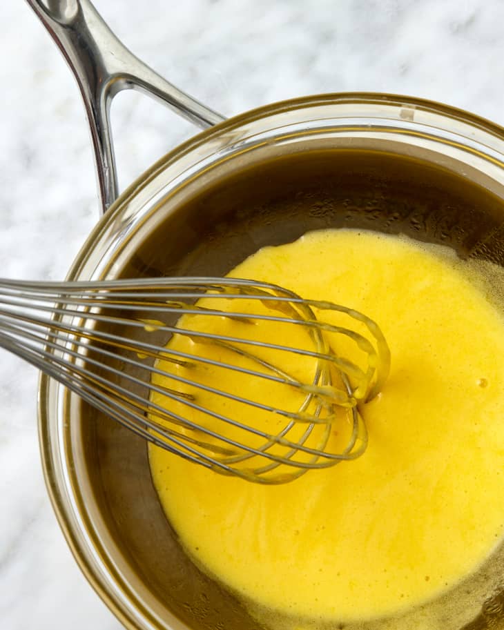 someone whisking hollandaise in a glass bowl