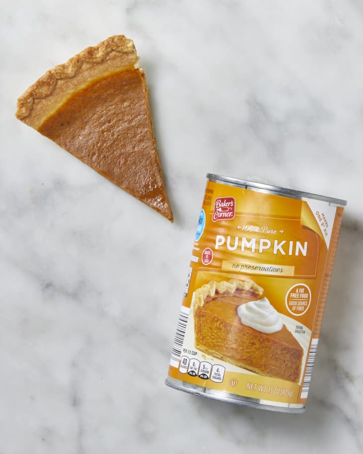 Can of Aldi Pumpkin Puree with a slice of pumpkin pie next to it on a marble surface.