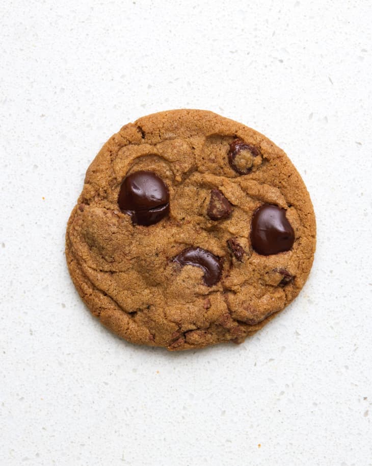Overhead view of a chocolate chip cookie on a white stone surface.