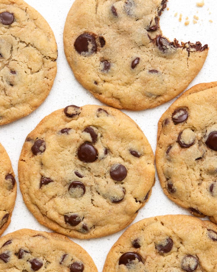 Overhead view of chocolate chip cookies on a white stone surface and cookie in the top right corner has a bite taken out of it.