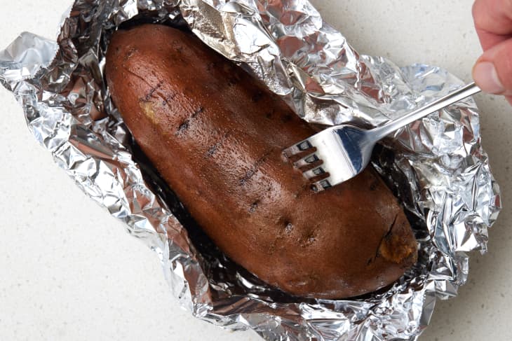 Overhead view of a baked sweet potato resting in tin foil with a fork going into it.