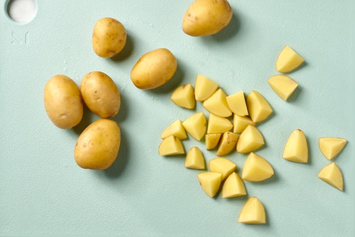 Overhead view of some whole potatoes, as well as some cut into small pieces on a light blue cutting board.