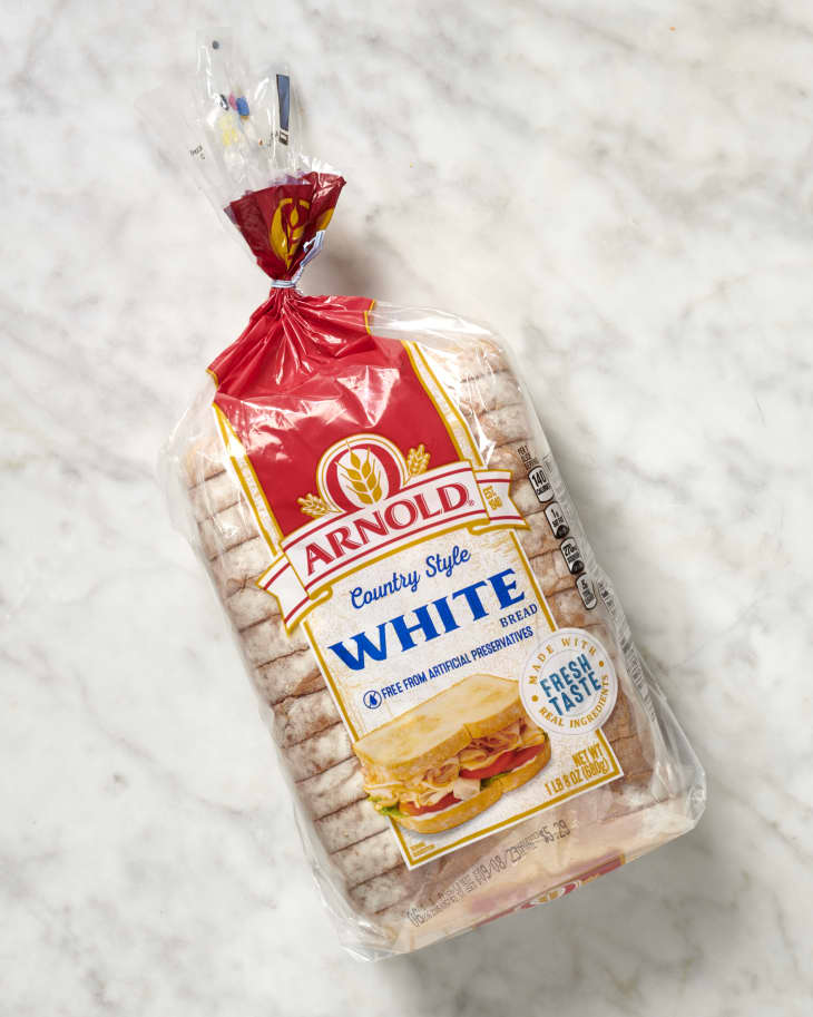 Overhead view of a loaf of Arnold brand country style white bread still in the original packaging, on a marble surface.
