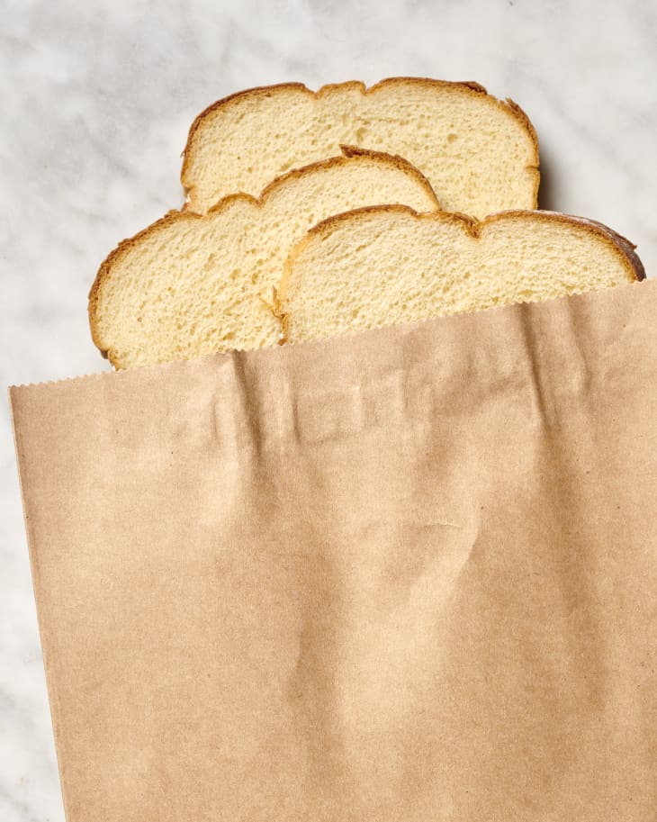 Overhead view of three slices of bread peeking out of the top of a brown paper bag.