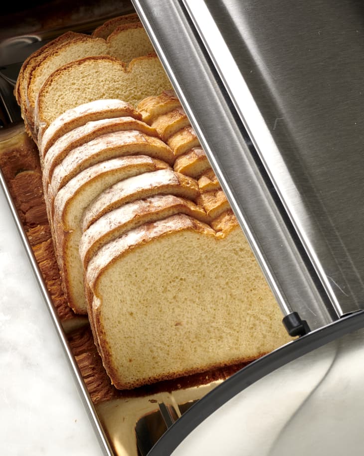 Overhead view of ten slices of white bread in a metal bread box with the lid open.