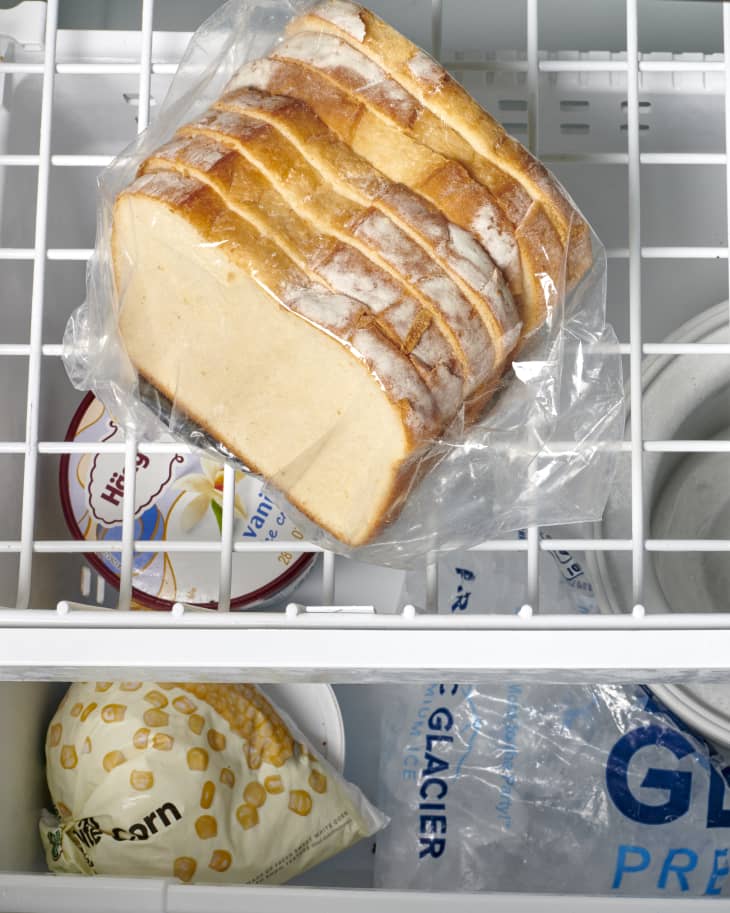 Overhead view of seven slices of white bread wrapped in plastic on the top drawer of a freezer.