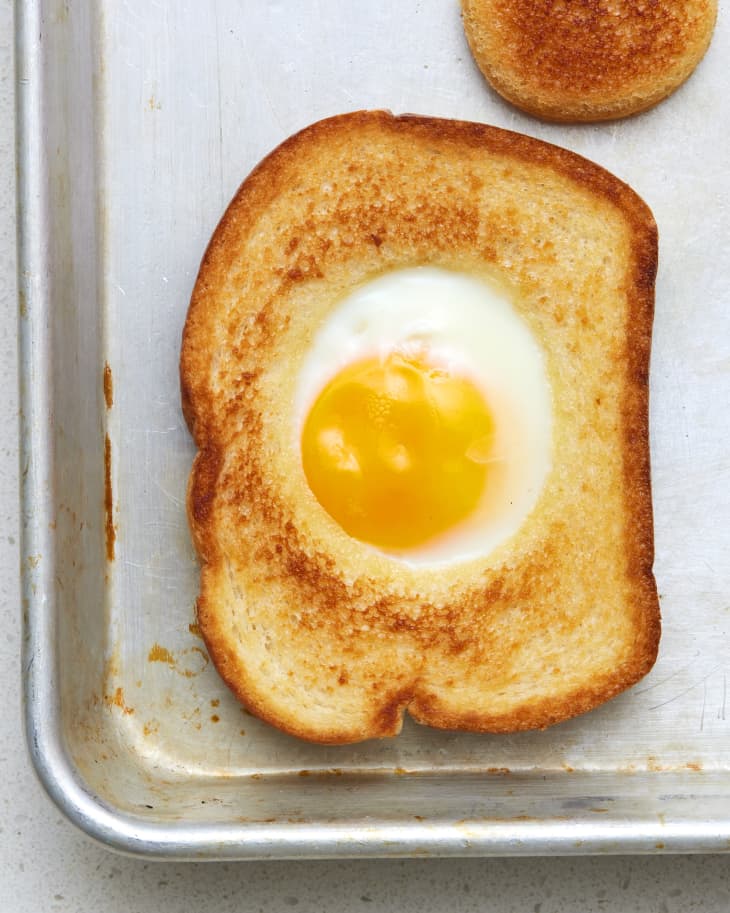 Egg-in-a-hole on a baking sheet with the bread hole next to it.