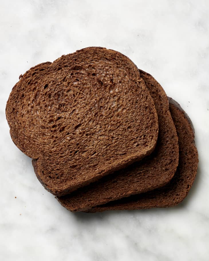 Overhead view of three slices of pumpernickel bread on a marble surface.