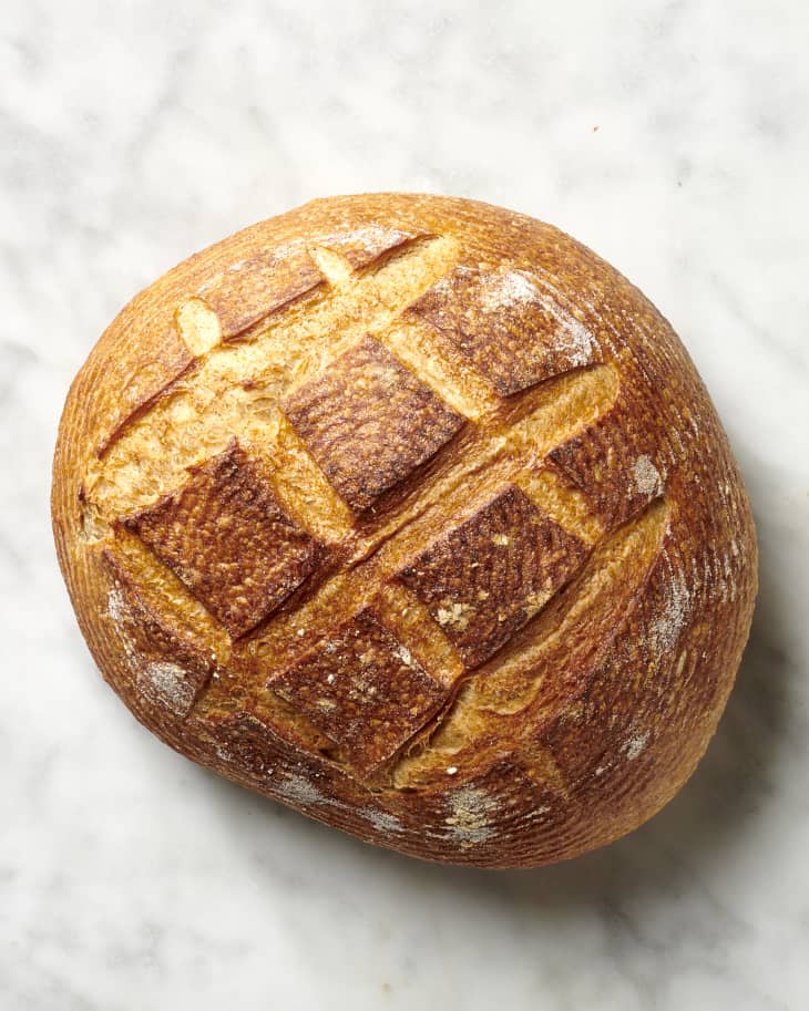 Overhead view of a round loaf of sourdough bread on a marble surface.
