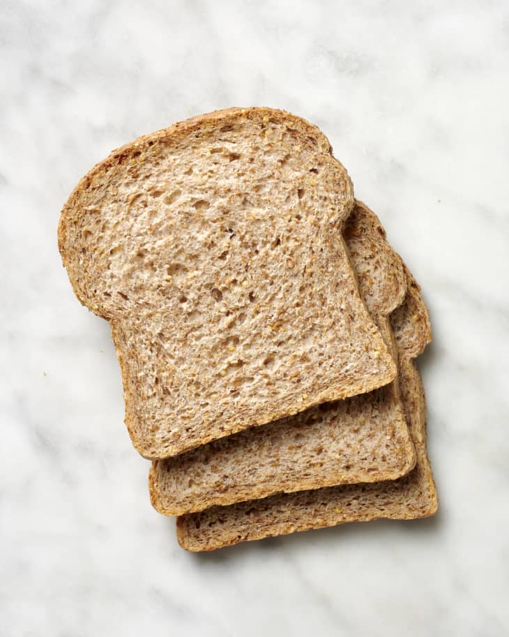 Overhead view of three slices of sprouted grain bread on a marble surface.